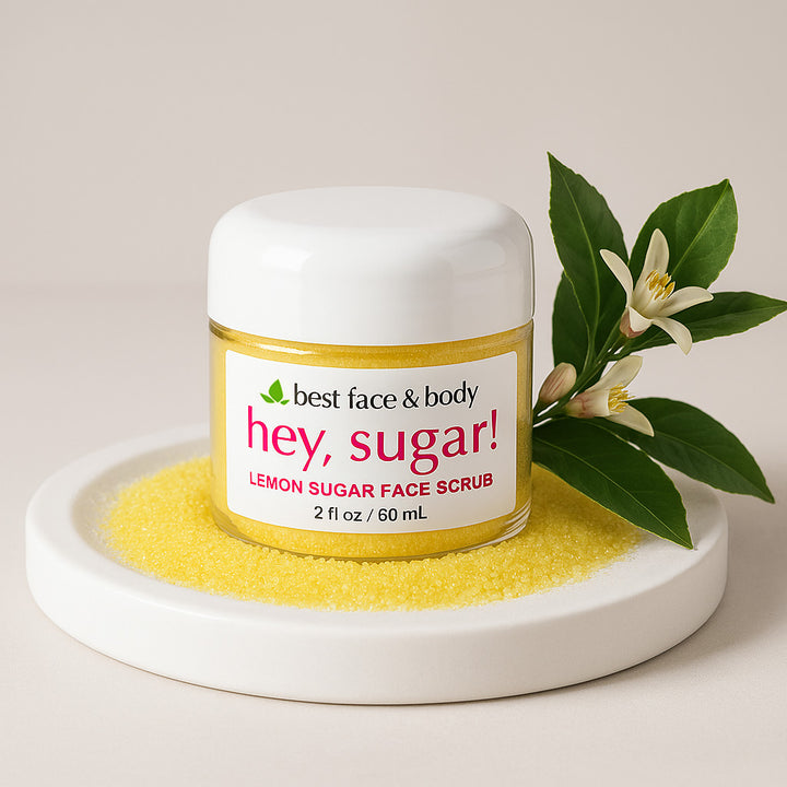 A container of 'Hey, Sugar! Lemon Sugar Face Scrub' by Best Face & Body, surrounded by dried lemon sugar scrubby bits and floral elements.