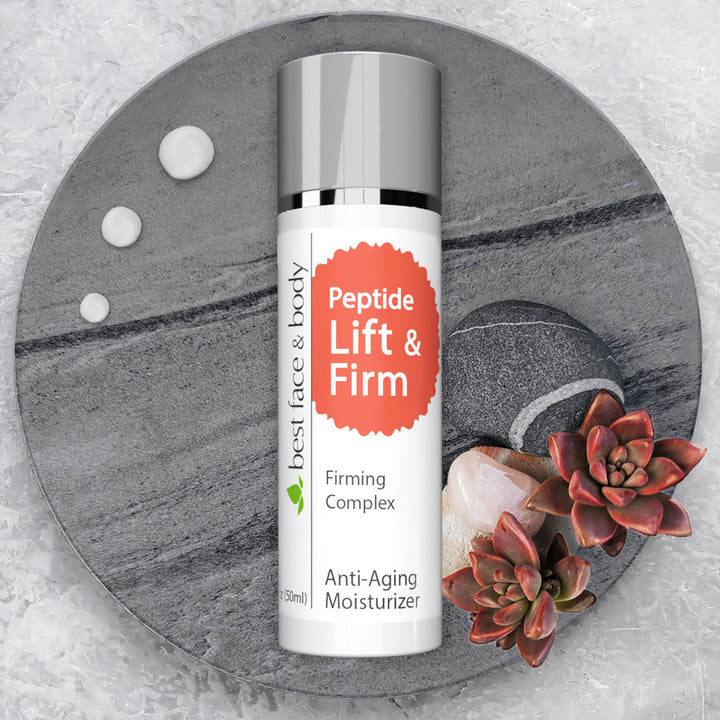 A pump bottle of Peptide Lift & Firm firming complex cream placed on a grey surface with a few drops around it, alongside red succulent florets