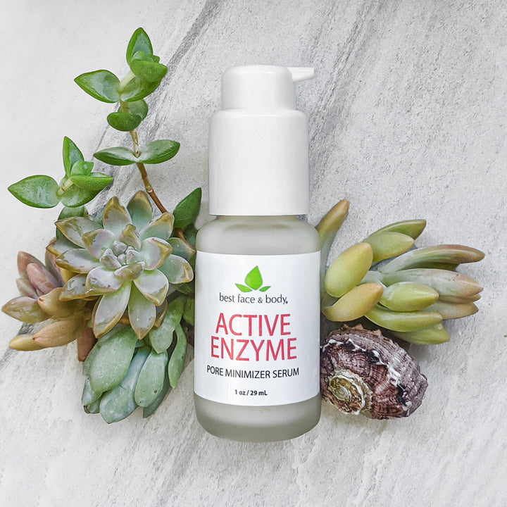 Active Enzyme Pore Minimizer Serum 1 oz frosted glass bottle with white pump top, photographed on a grey stone background with succulents