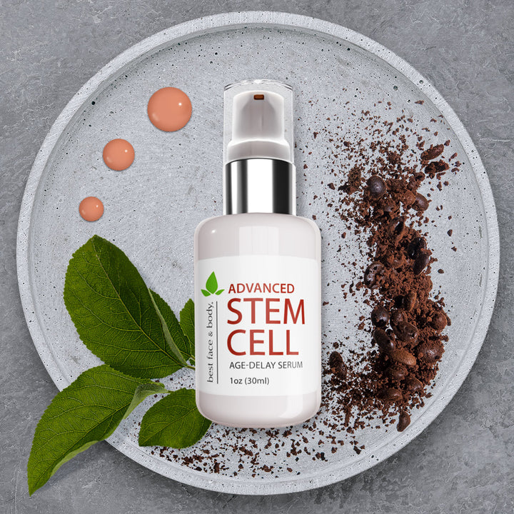 Advanced Stem Cell Age Delay Serum. 1oz glass bottle with pump top and silver ring. Pictured on shallow stone dish with coffee grounds, green leaves and orange-pink serum droplets in background.