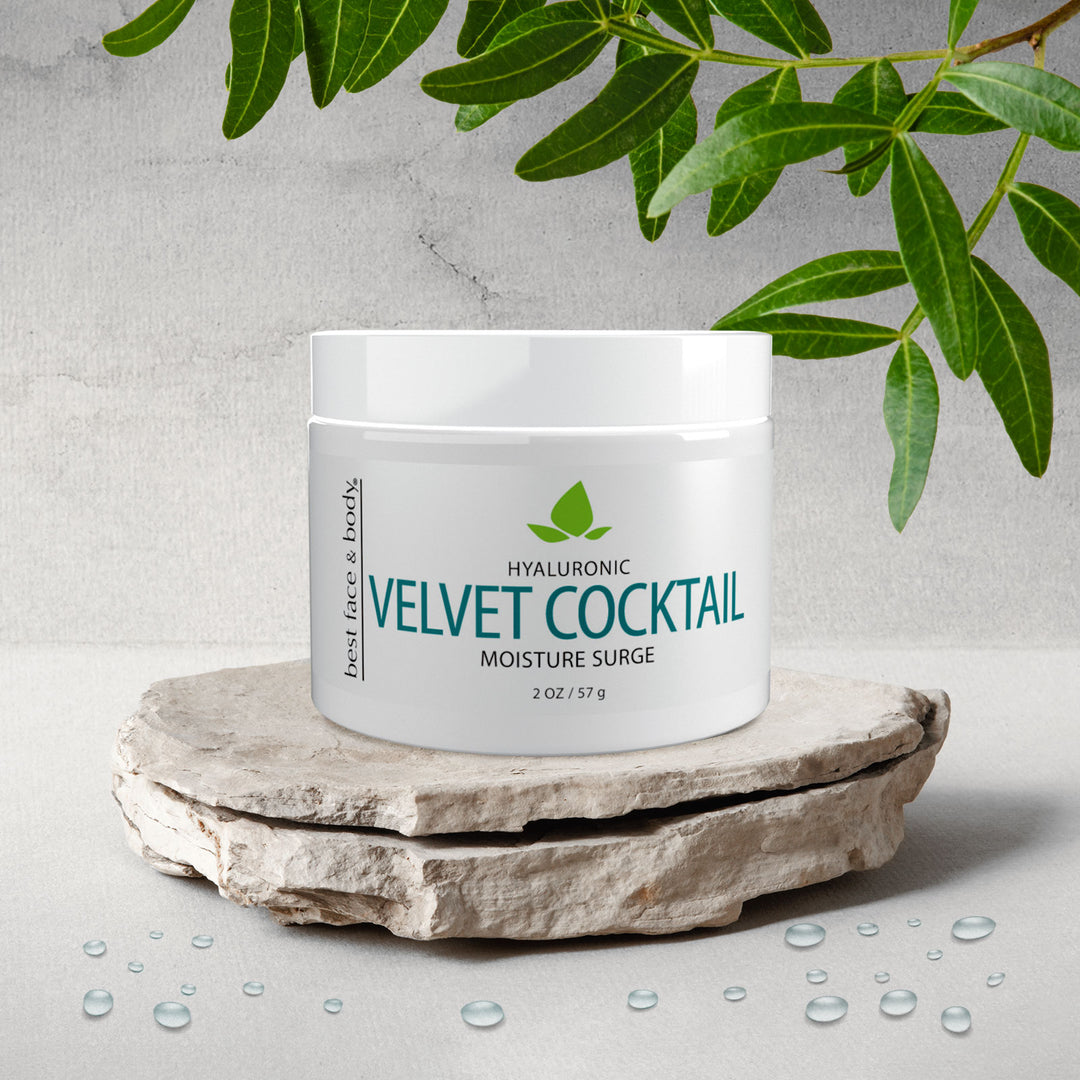 A white jar labeled 'Hyaluronic Velvet Cocktail Moisture Surge' is placed on a natural stone, with water droplets scattered around, and leaves in the background.