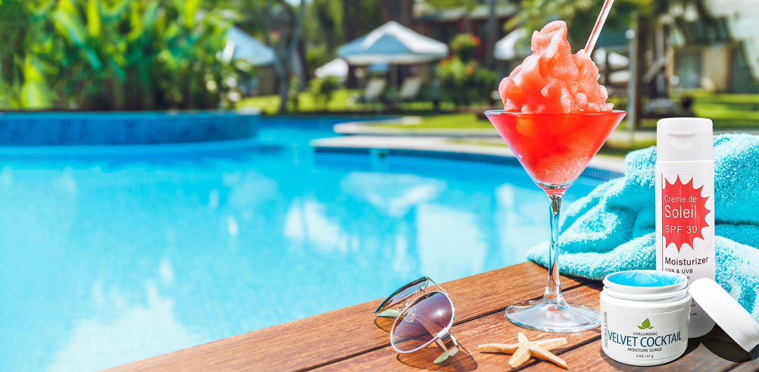 sunglasses, summer cocktail and SPF skincare products pictured in the foreground with a crystal blue pool in the background.