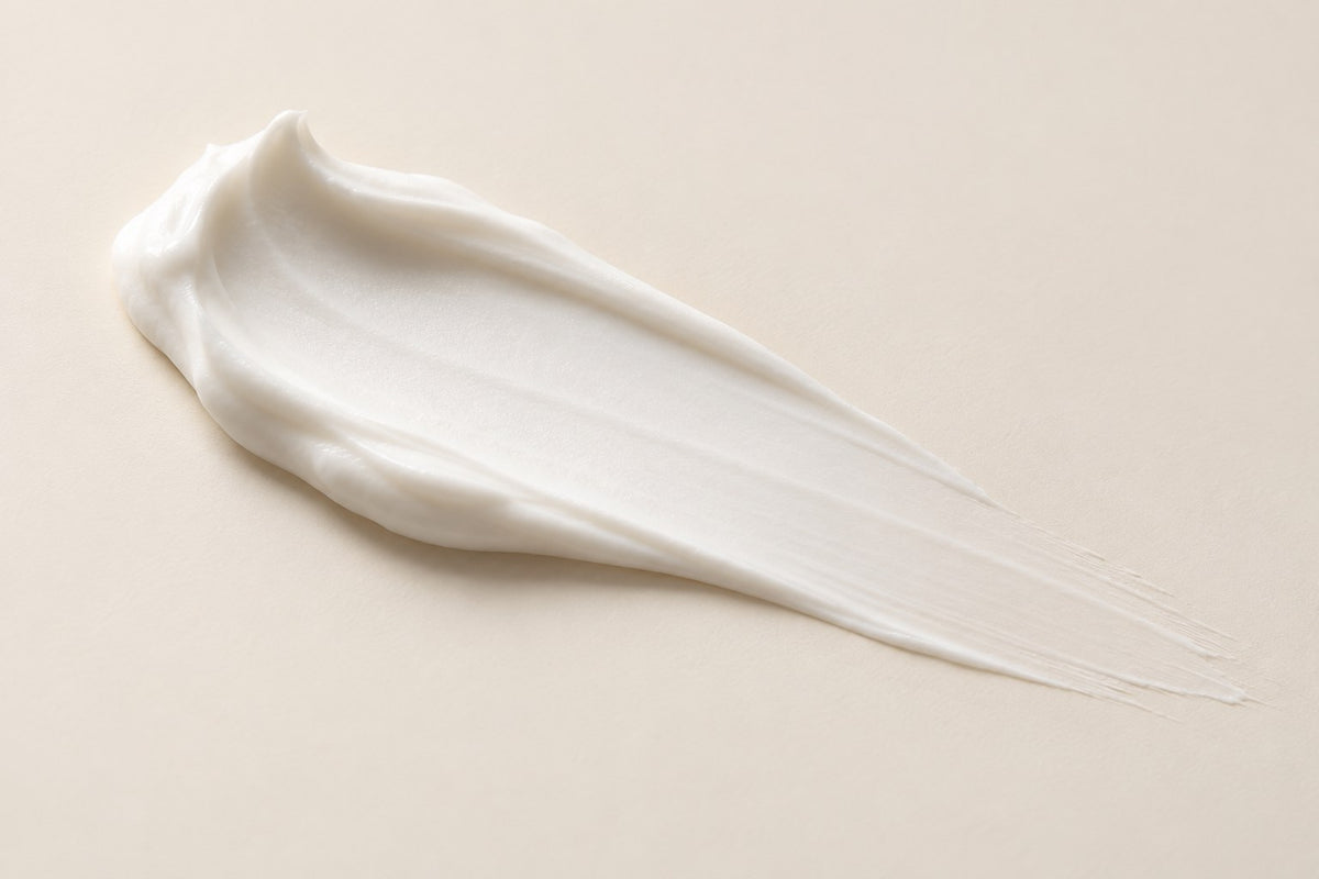 Swipe of silky white moisturizer cream on an ivory background