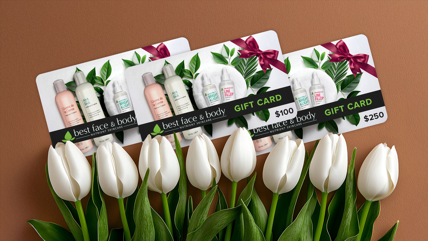 three 'best face & body gift cards' are displayed at an angle in the middle of the image which also features a row of white tulips lined up across the bottom. the background is a tan, textured surface.