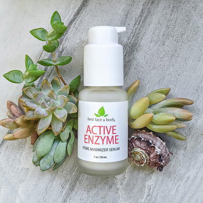 Active Enzyme Pore Minimizer Serum 1 oz frosted glass bottle with white pump top, photographed on a grey stone background with succulents