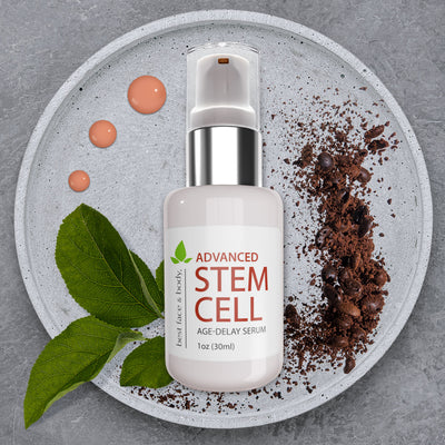 Advanced Stem Cell Age Delay Serum. 1oz glass bottle with pump top and silver ring. Pictured on shallow stone dish with coffee grounds, green leaves and orange-pink serum droplets in background.