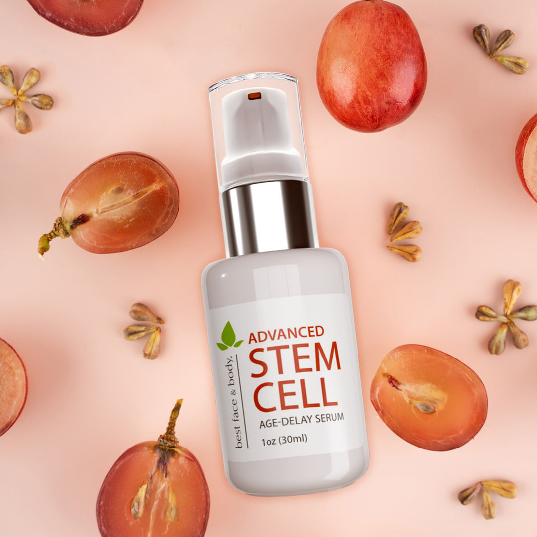bottle of Advanced Stem Cell Age-Delay serum pictured with sliced and whole grapes and grape seeds on a pale pink background